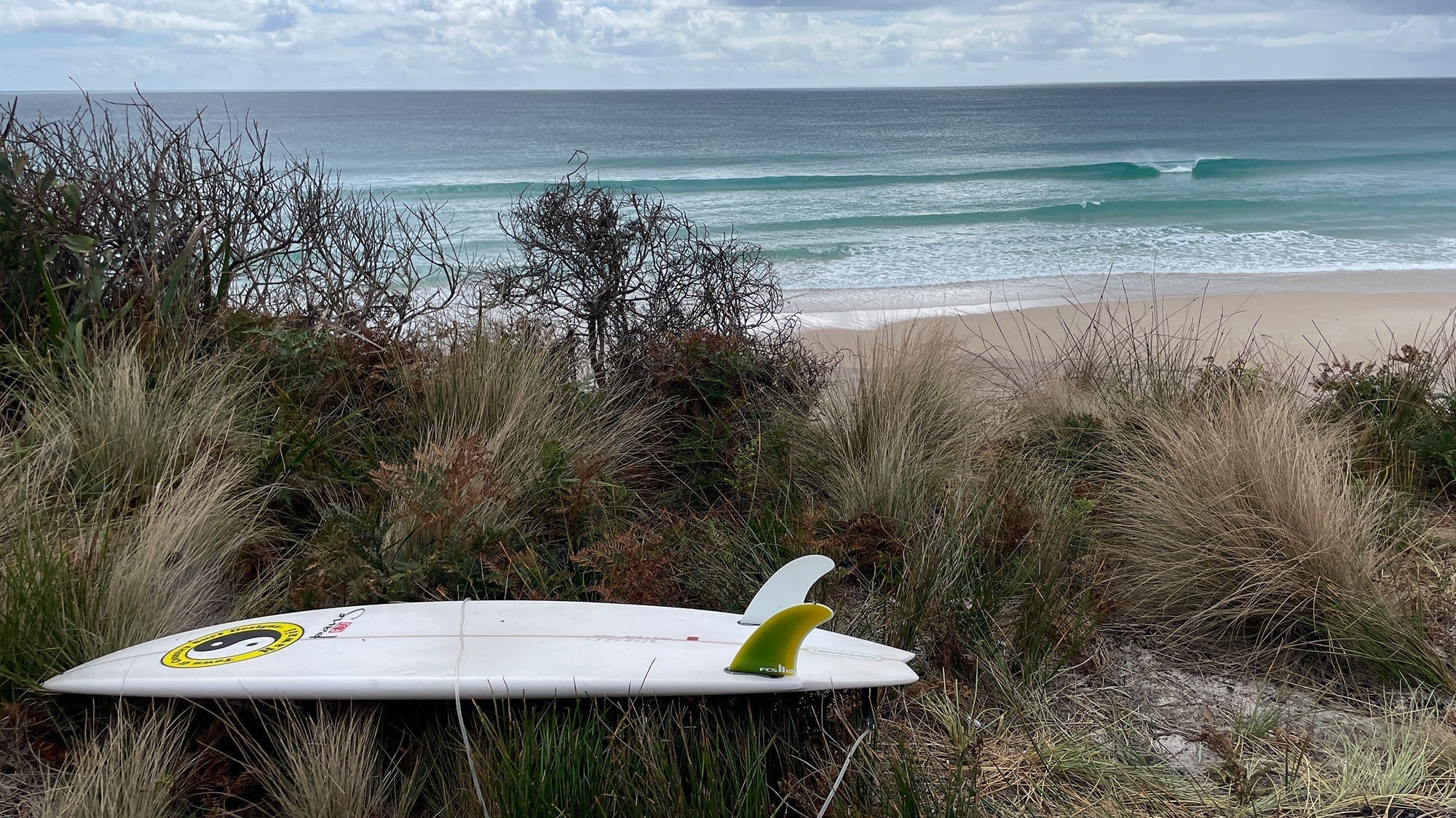 Surfboard on the sand with beach and waves in the background