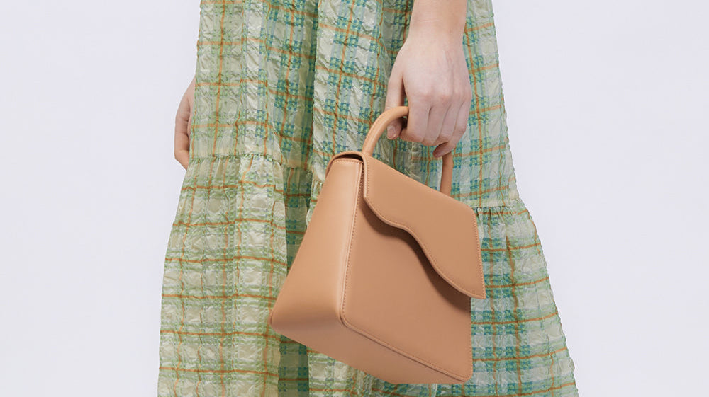 Person wearing a check green dress and holding a camel coloured bag