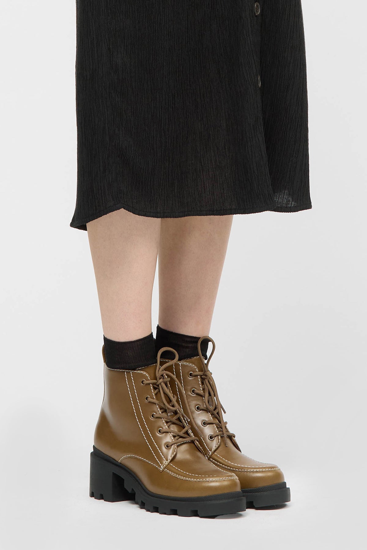 Woman wearing a lace up boot in olive with black sole