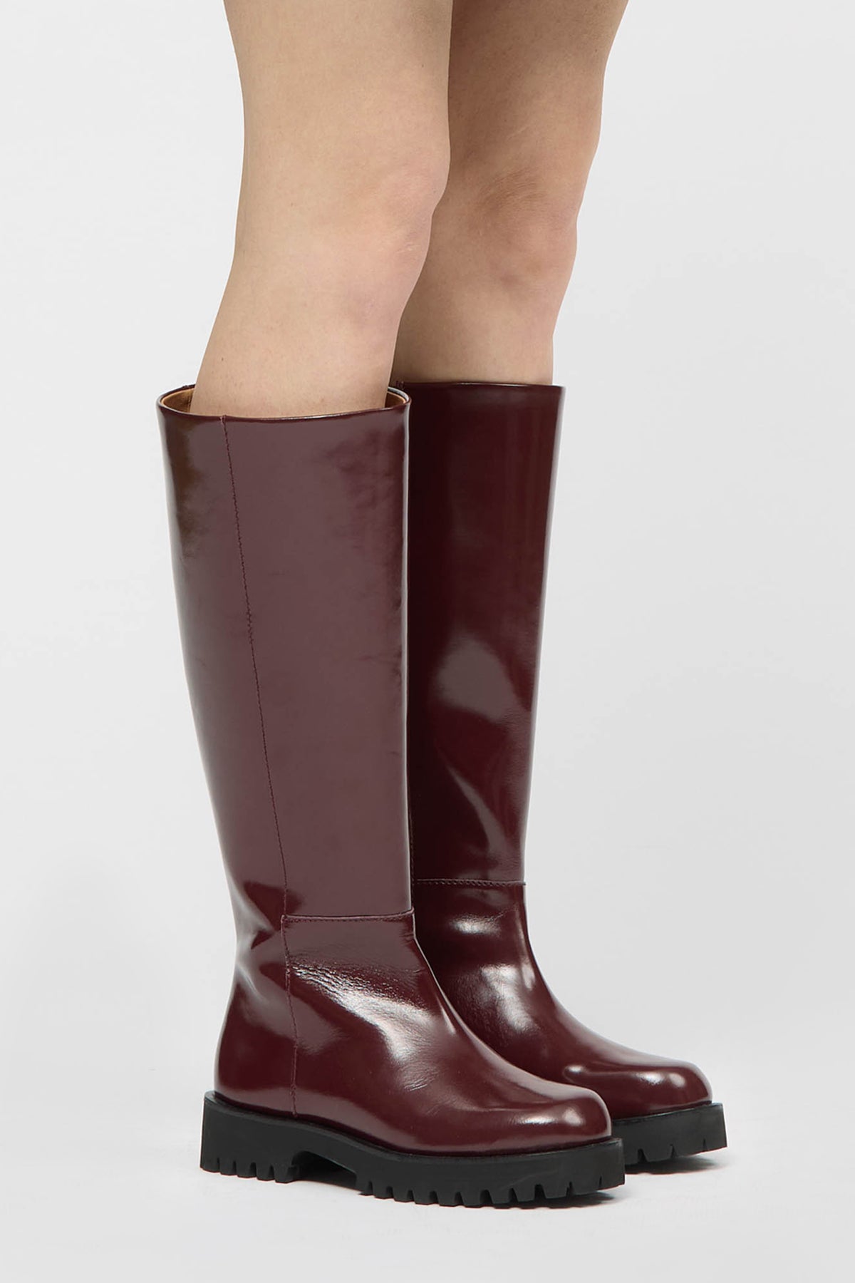 Knee high burgundy boot in a glossy material with a thick black sole