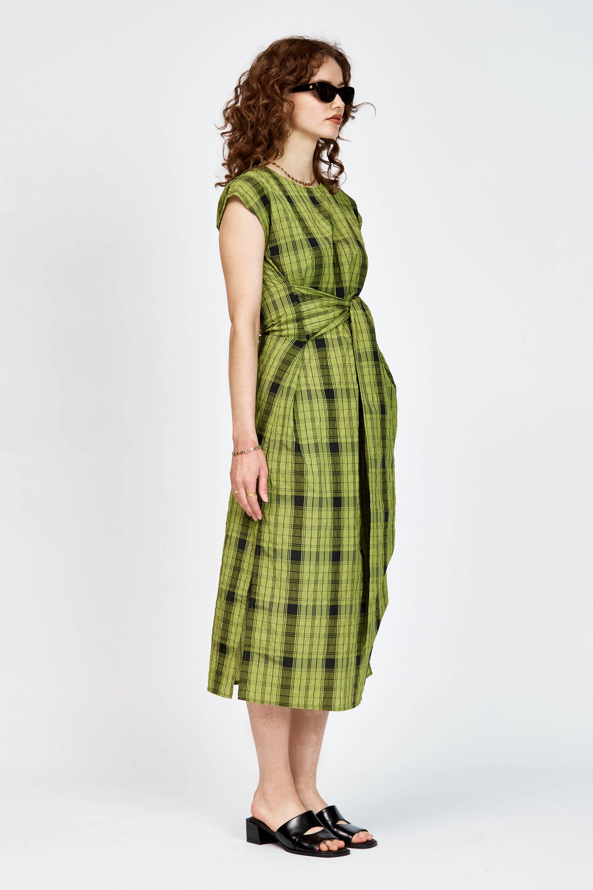Model wearing an olive and black check midi length dress with a tie waist detail