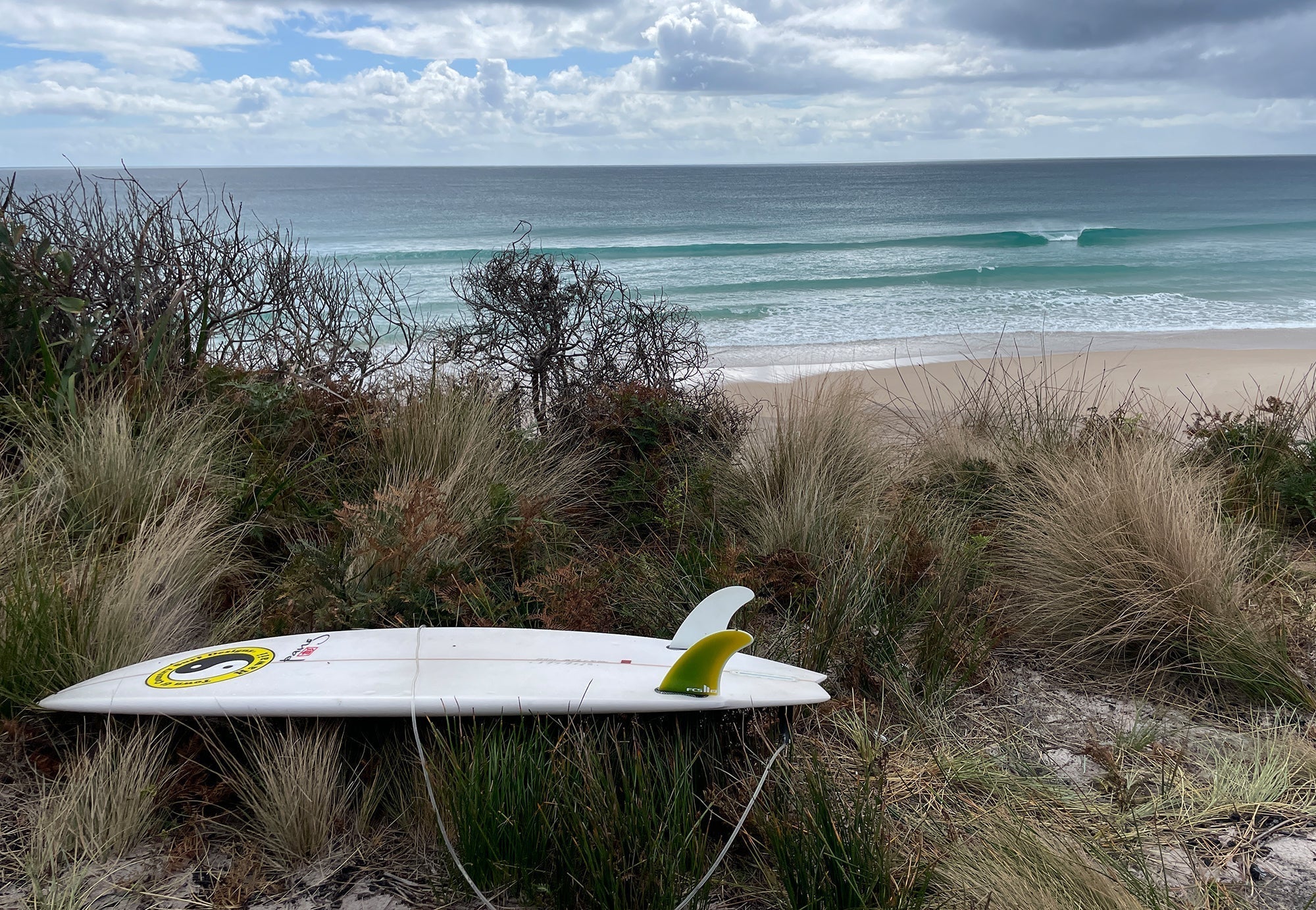 Surfboard on the sand with beach and waves in the background