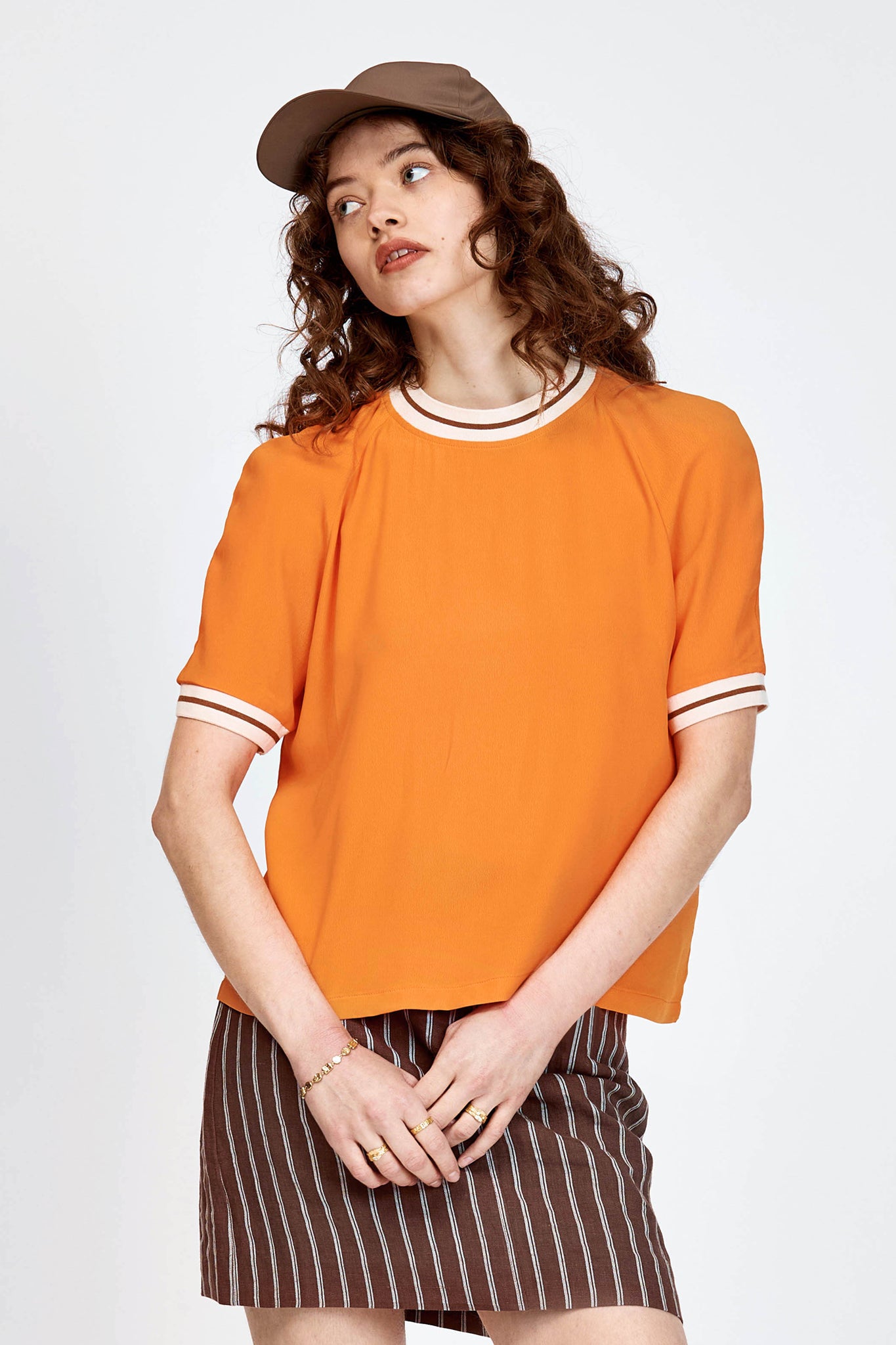 Model wearing orange top with white stripe detailing along neckline and armholes