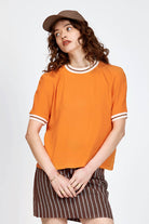 Model wearing orange top with white stripe detailing along neckline and armholes