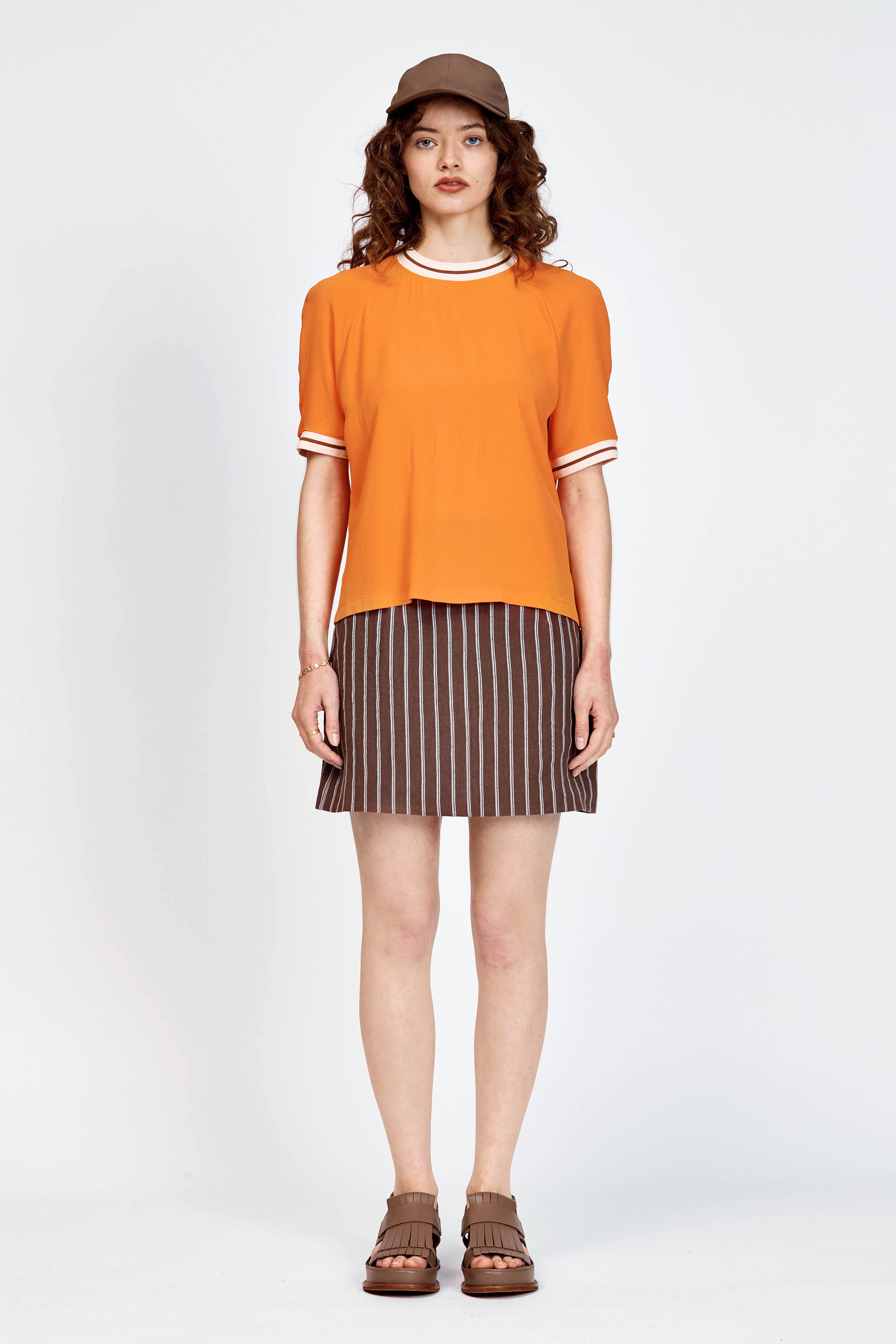 Model wearing orange top with white stripe detailing along neckline and armholes