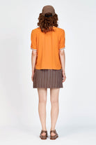 Model wearing orange top with white stripe detailing along neckline and armholes