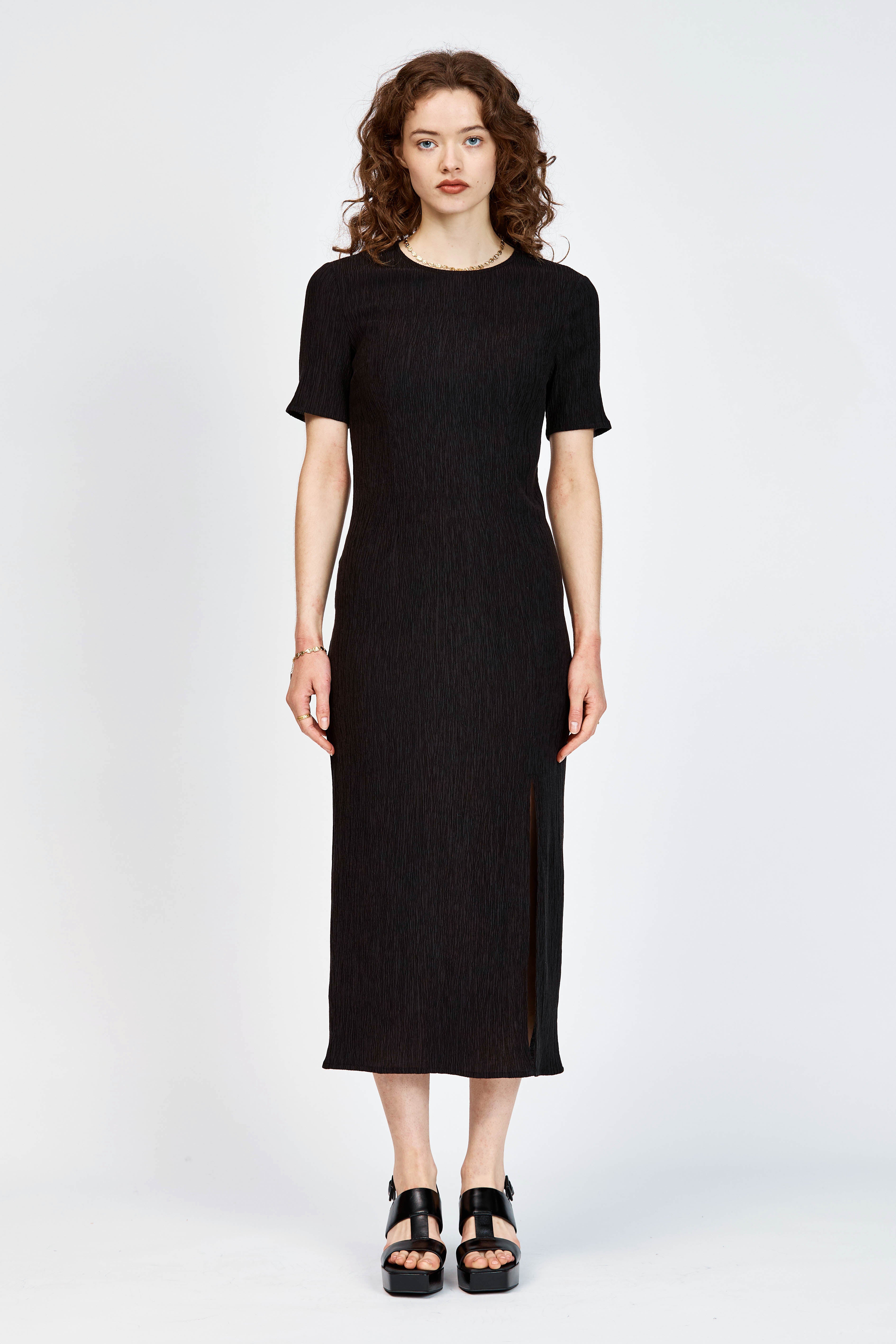 Model wearing a black short sleeve midi length dress with side slit