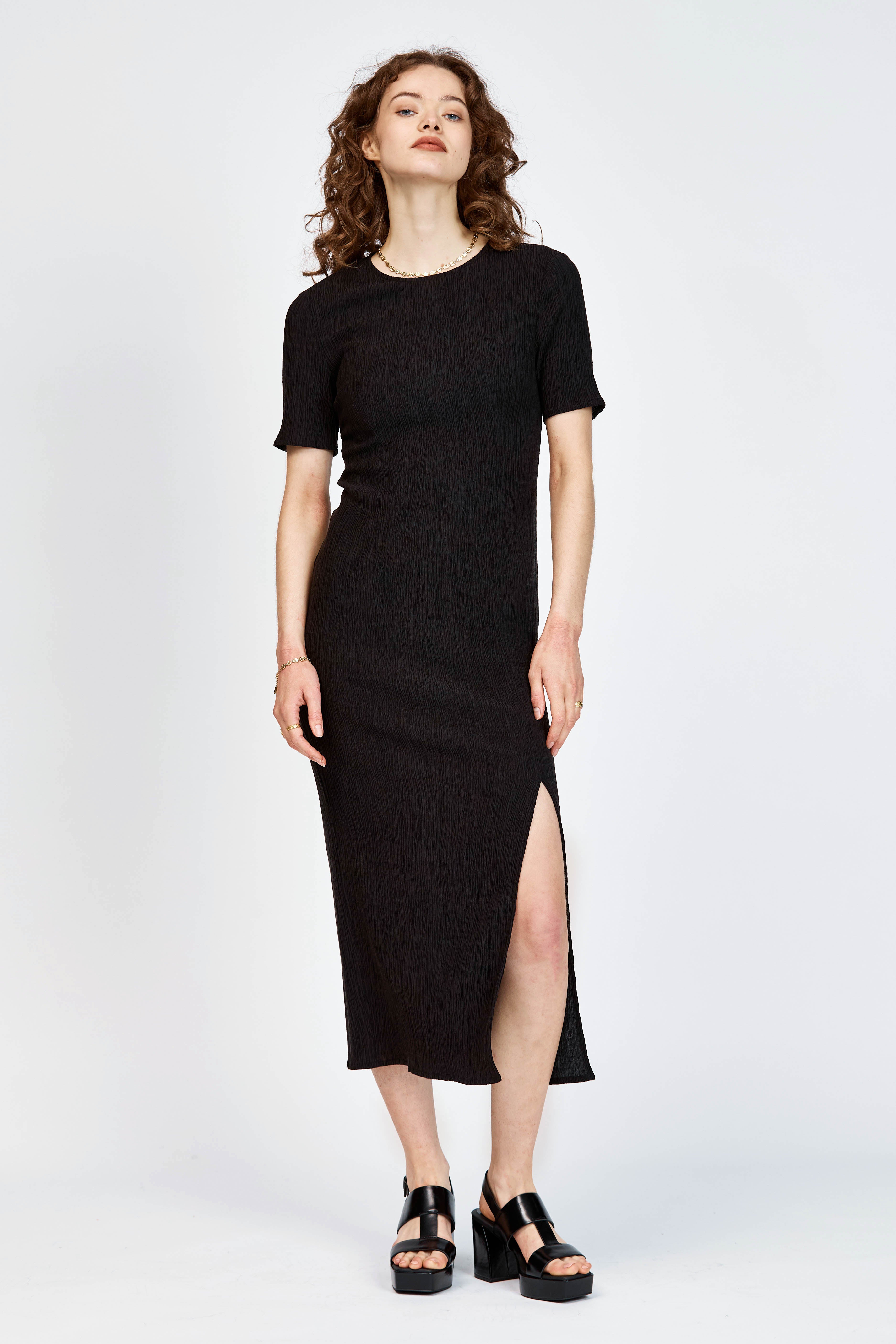 Model wearing a black short sleeve midi length dress with side slit