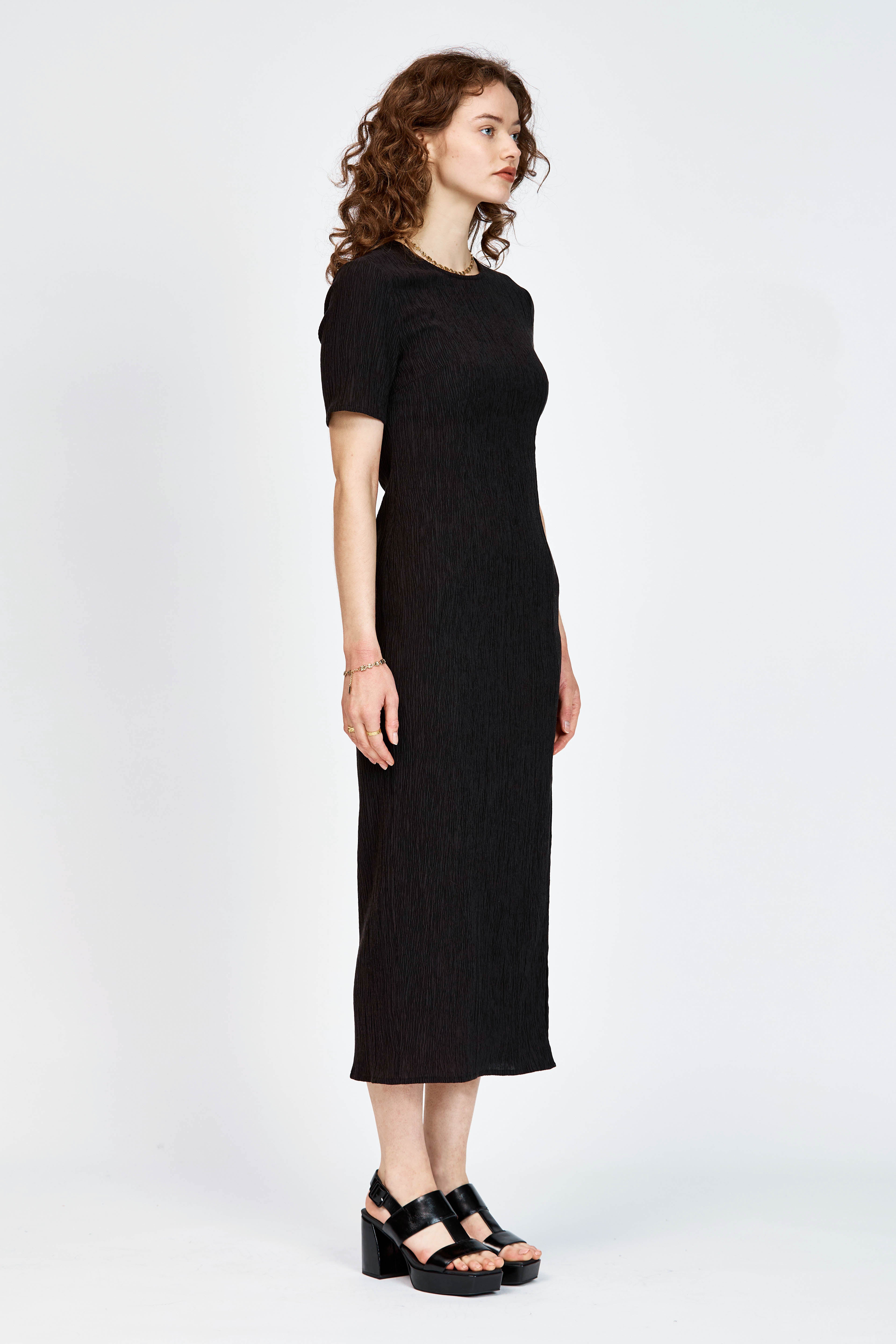 Model wearing a black short sleeve midi length dress with side slit