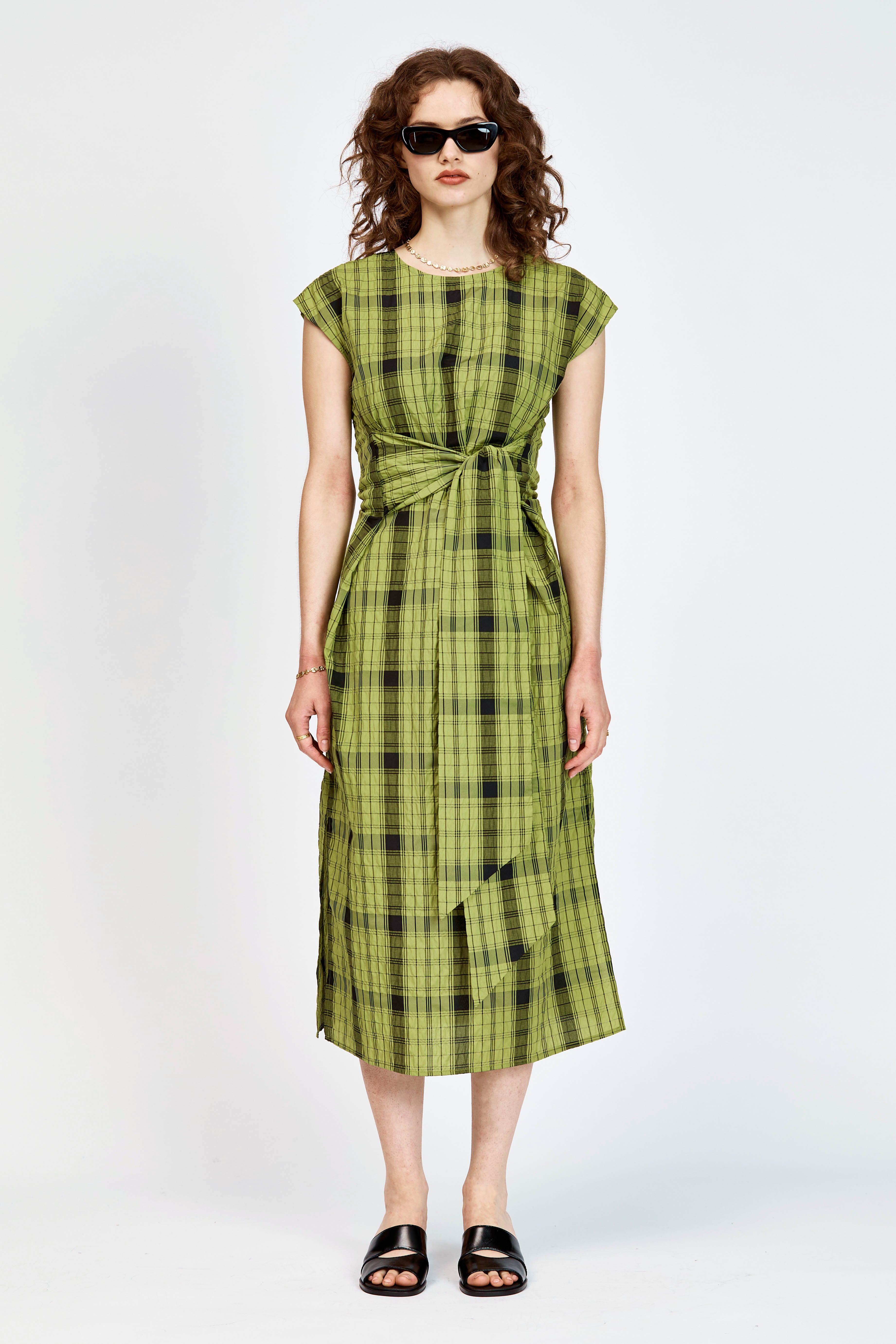 Model wearing an olive and black check midi length dress with a tie waist detail