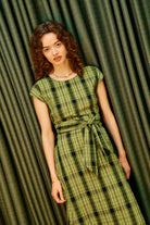 Model wearing an olive an black check midi length dress with a tie waist detail